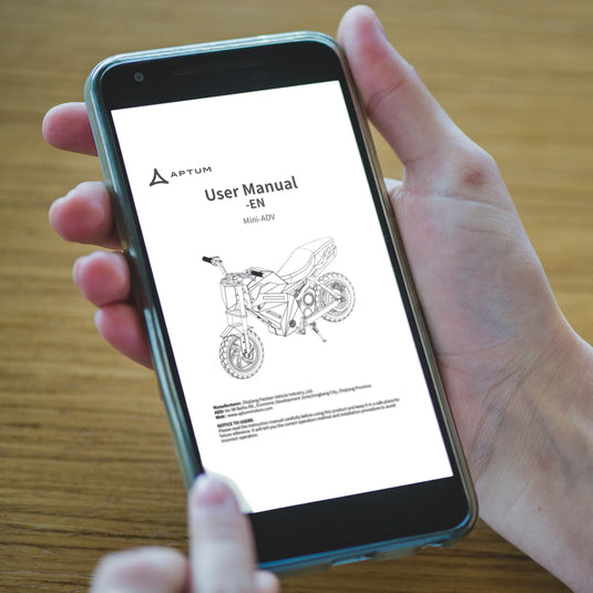 Hand holding a smartphone displaying a motorcycle user manual on a wooden surface